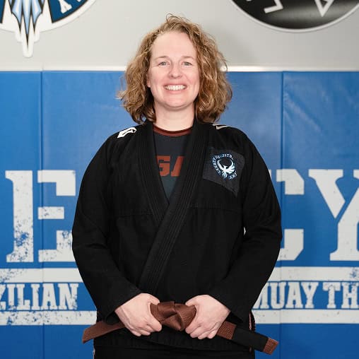 Experienced female BJJ instructor in gi, smiling confidently in training facility.
